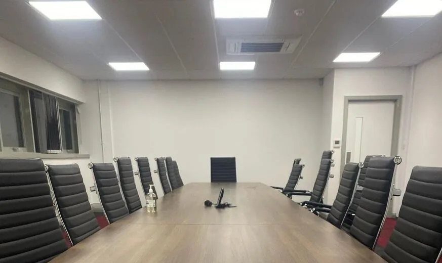 A boardroom lit by recessed LED ceiling panels, with the conference table and chairs below them